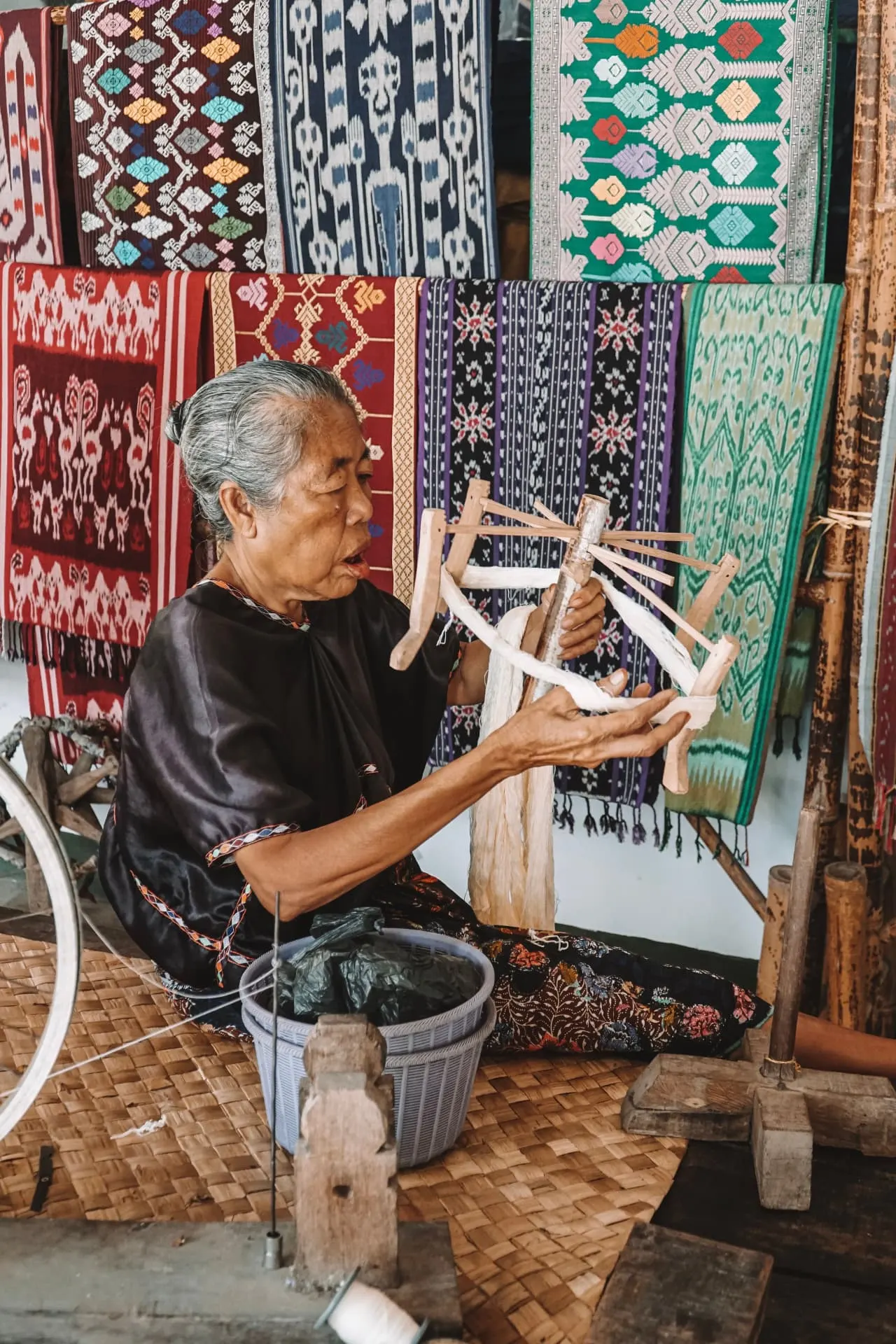 Elderly woman winding thread in front of handwoven ikat textiles