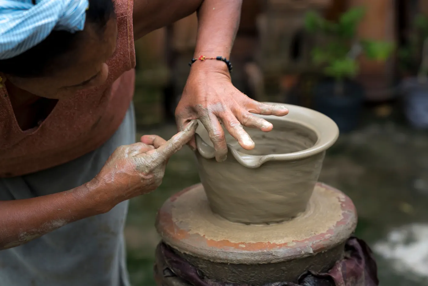 Hands shaping a clay pot on a traditional potter's wheel