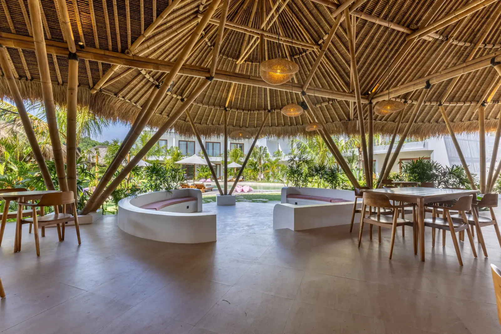 Open-air lounge and dining tables under the bamboo roof, the pool beyond