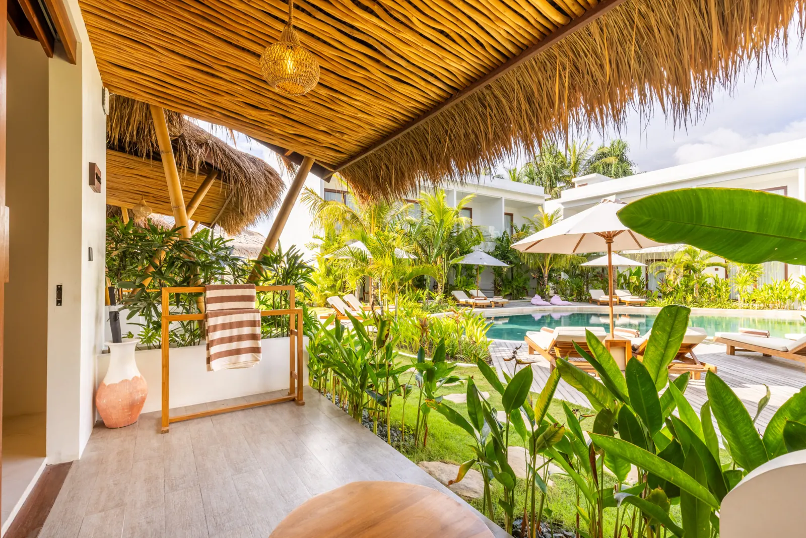 Furnished terrace under a thatched roof, overlooking the pool and garden