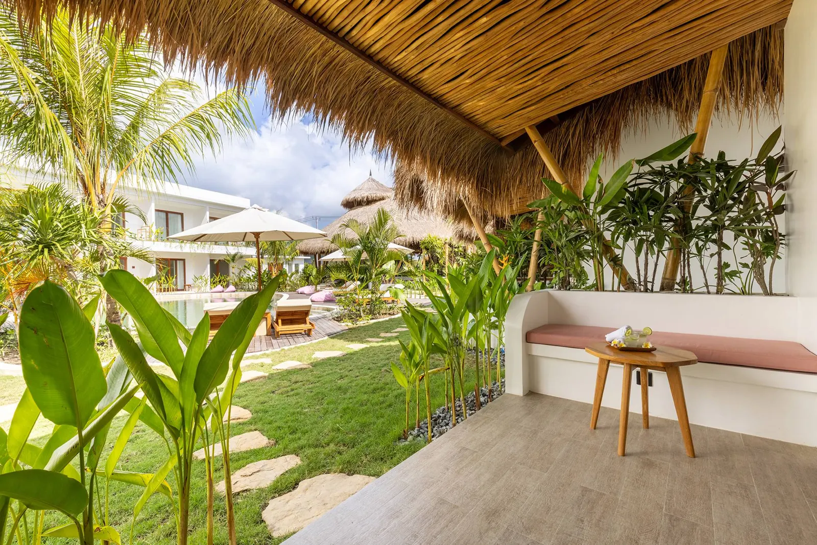 Bungalow terrace with built-in bench under a thatched roof, facing the garden