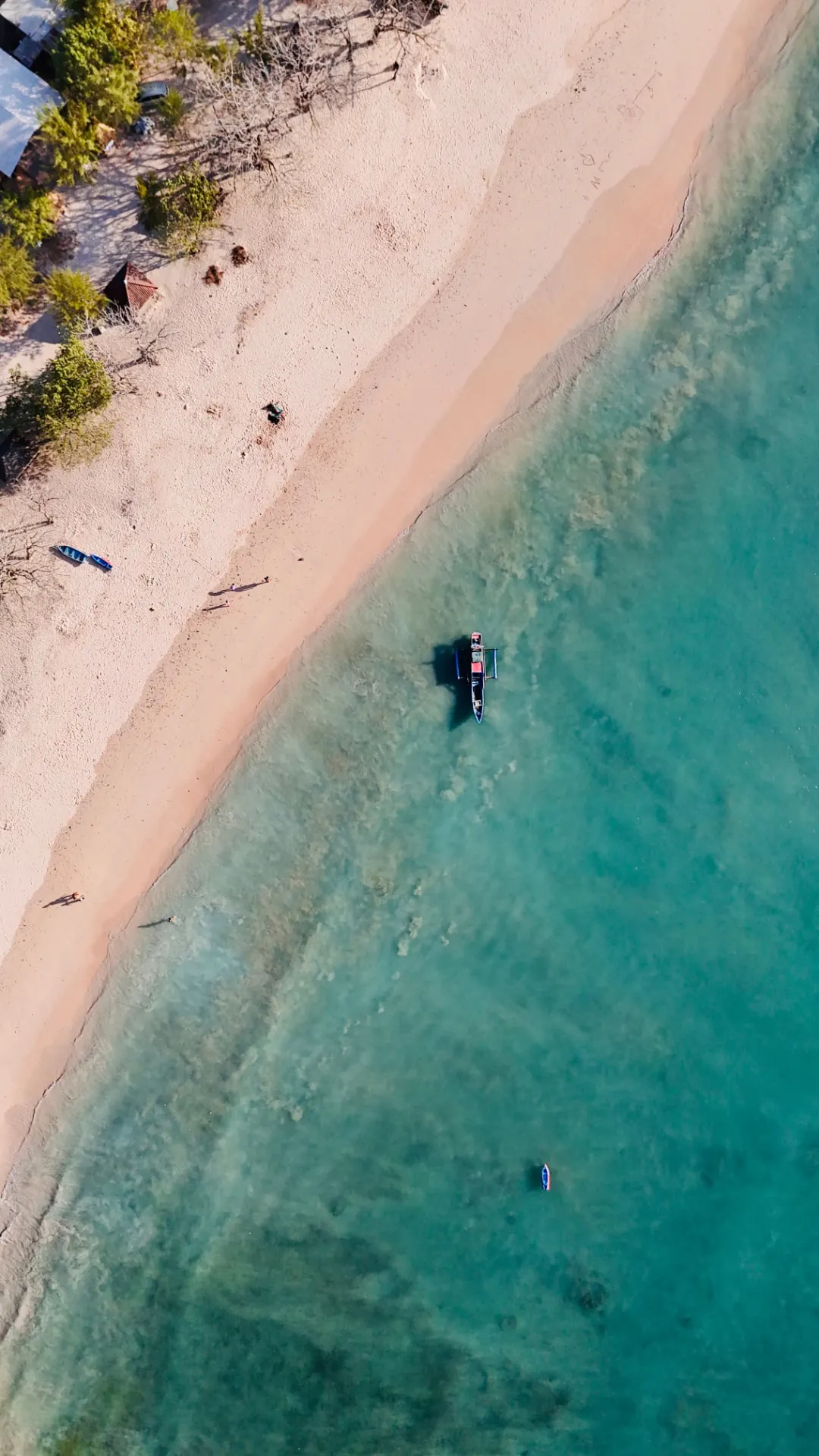 Aerial view of a pale pink sand beach and turquoise water with a moored outrigger boat