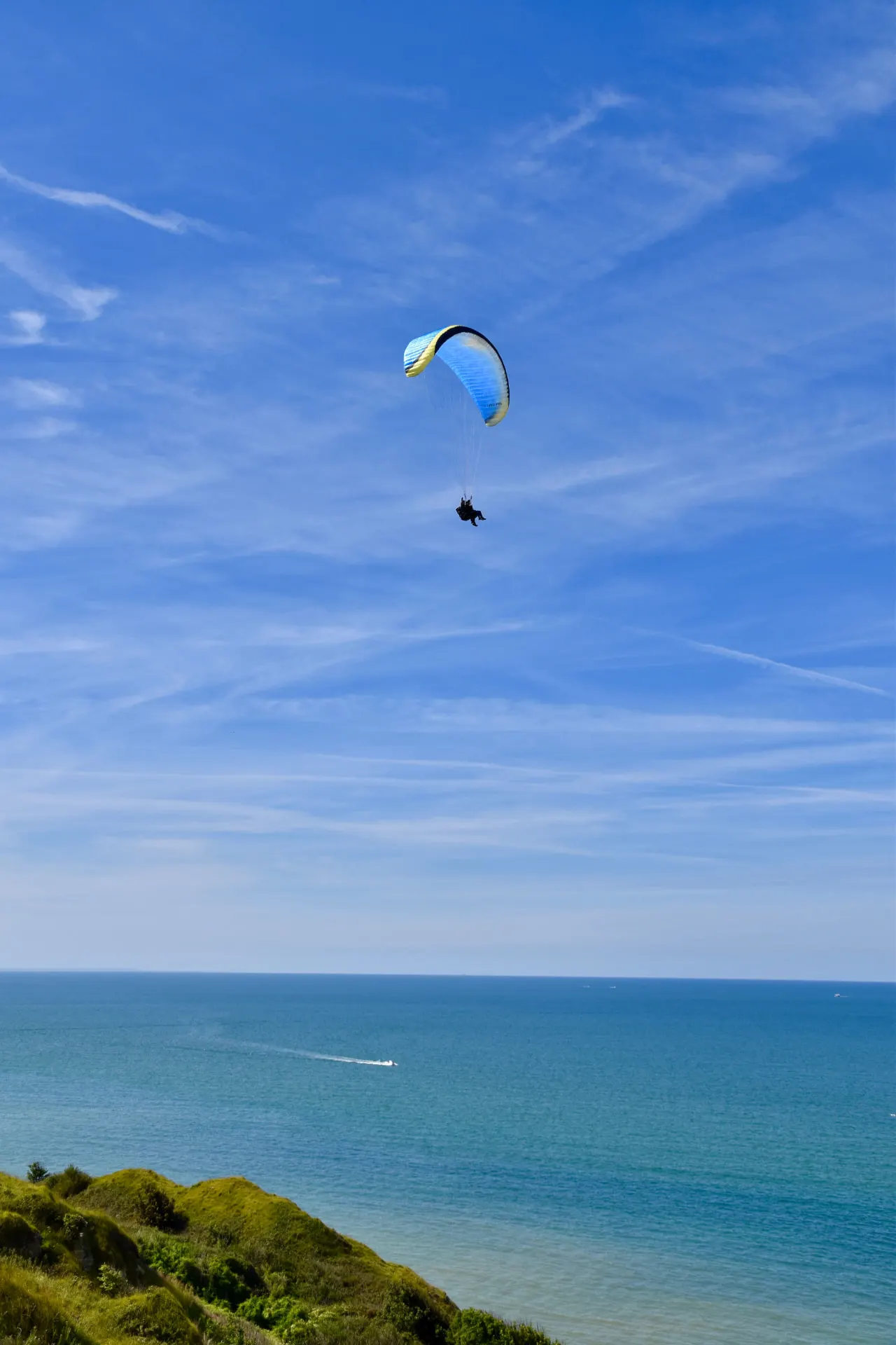 Paraglider flying in blue sky above the sea and a green coastal headland