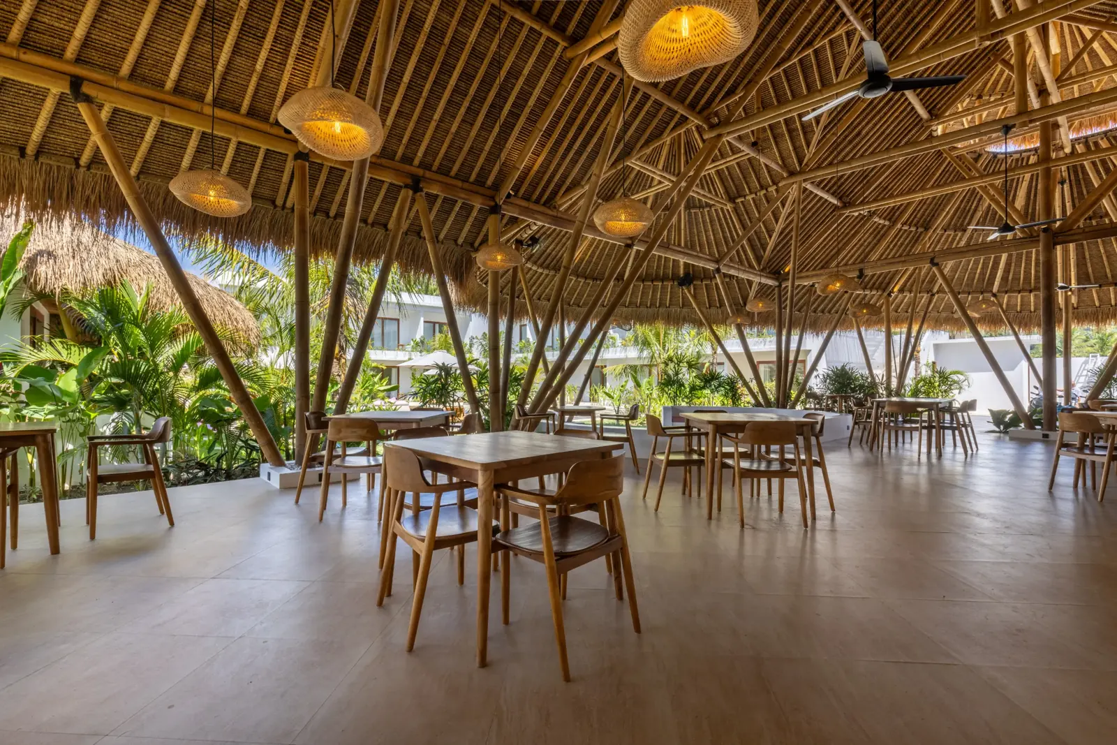 Wooden dining tables beneath woven pendant lamps and bamboo beams